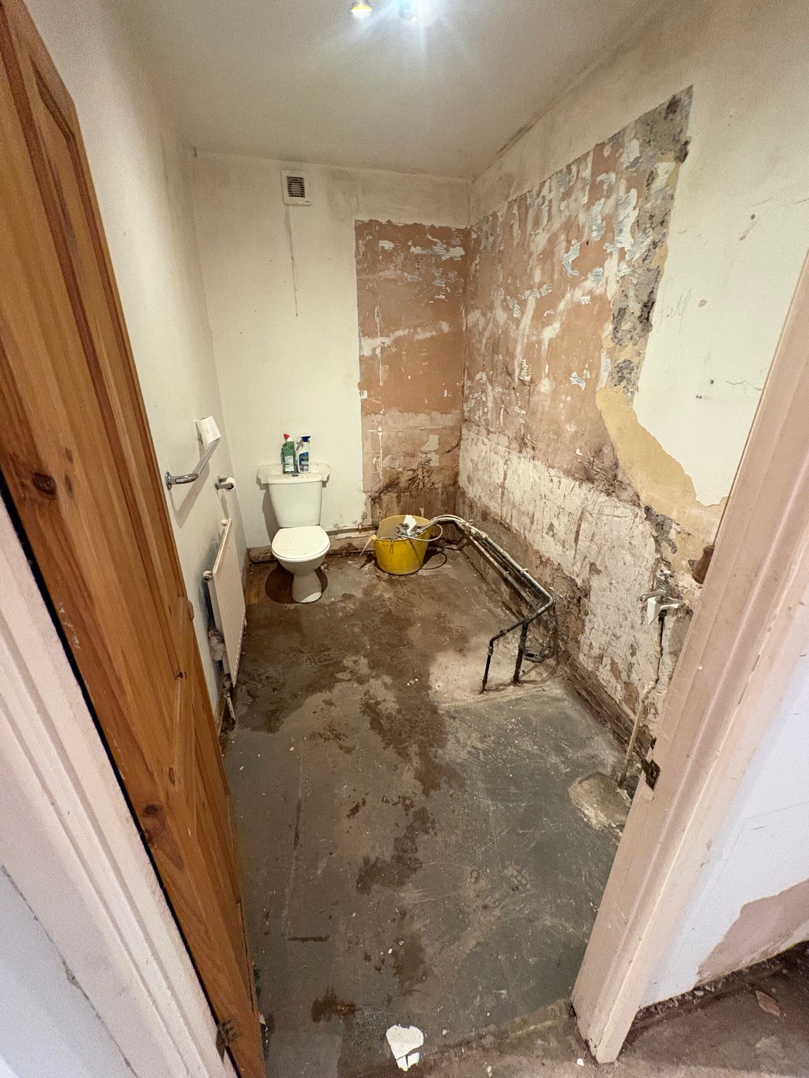 Bathroom during strip out with bath removed, pipework exposed and wall finishes being prepared