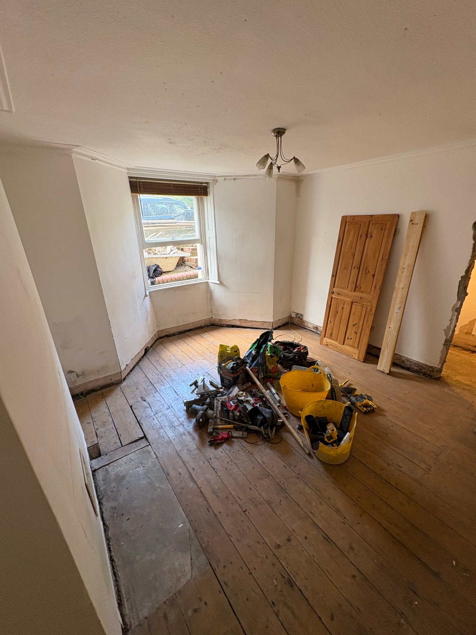 Lower ground floor room in Redland with exposed timber boards, removed skirting and staining around the bay window